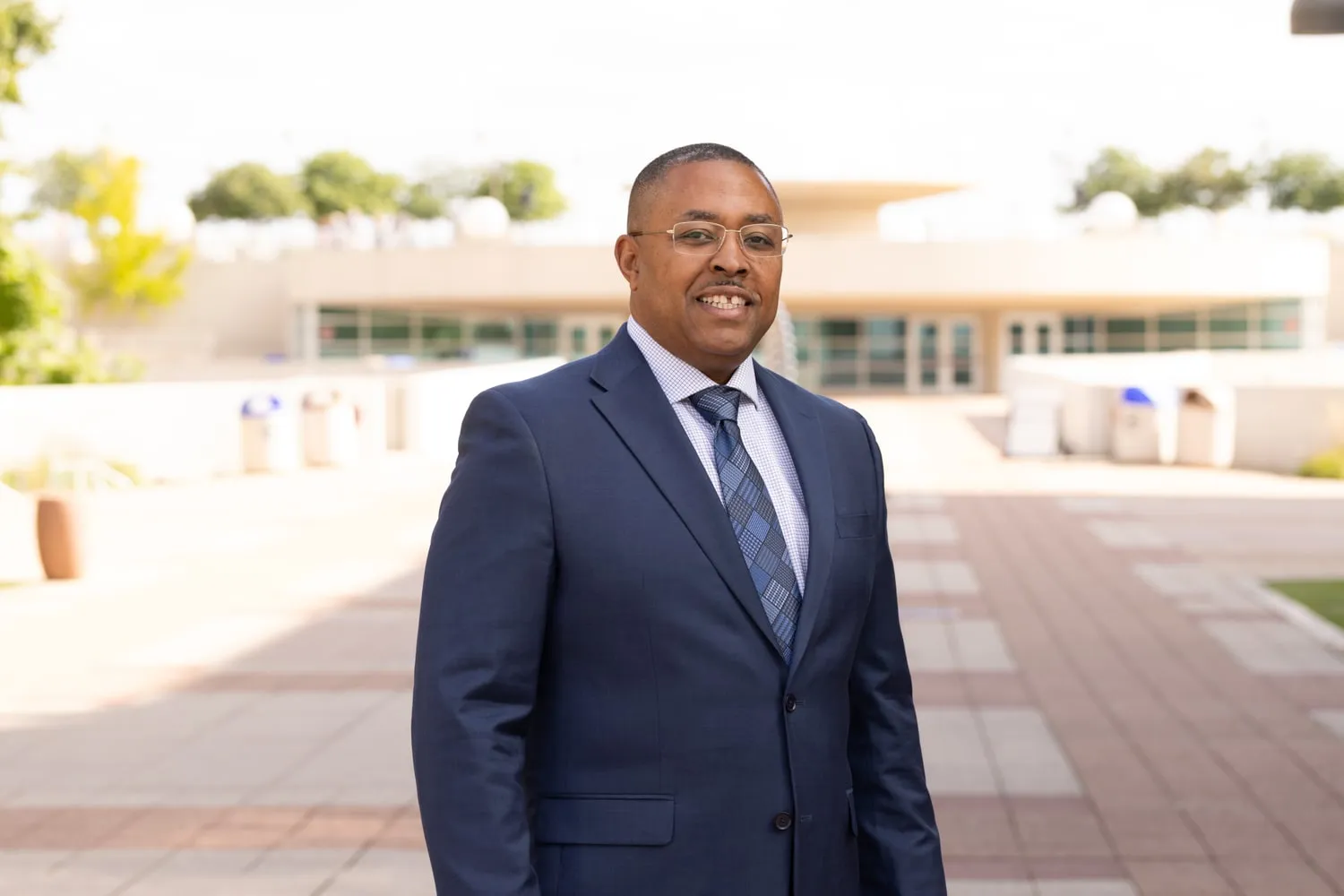 Kaleem Caire, candidate for Mayor of Madison, smiling in a navy suit and blue patterned tie outside Monona Terrace